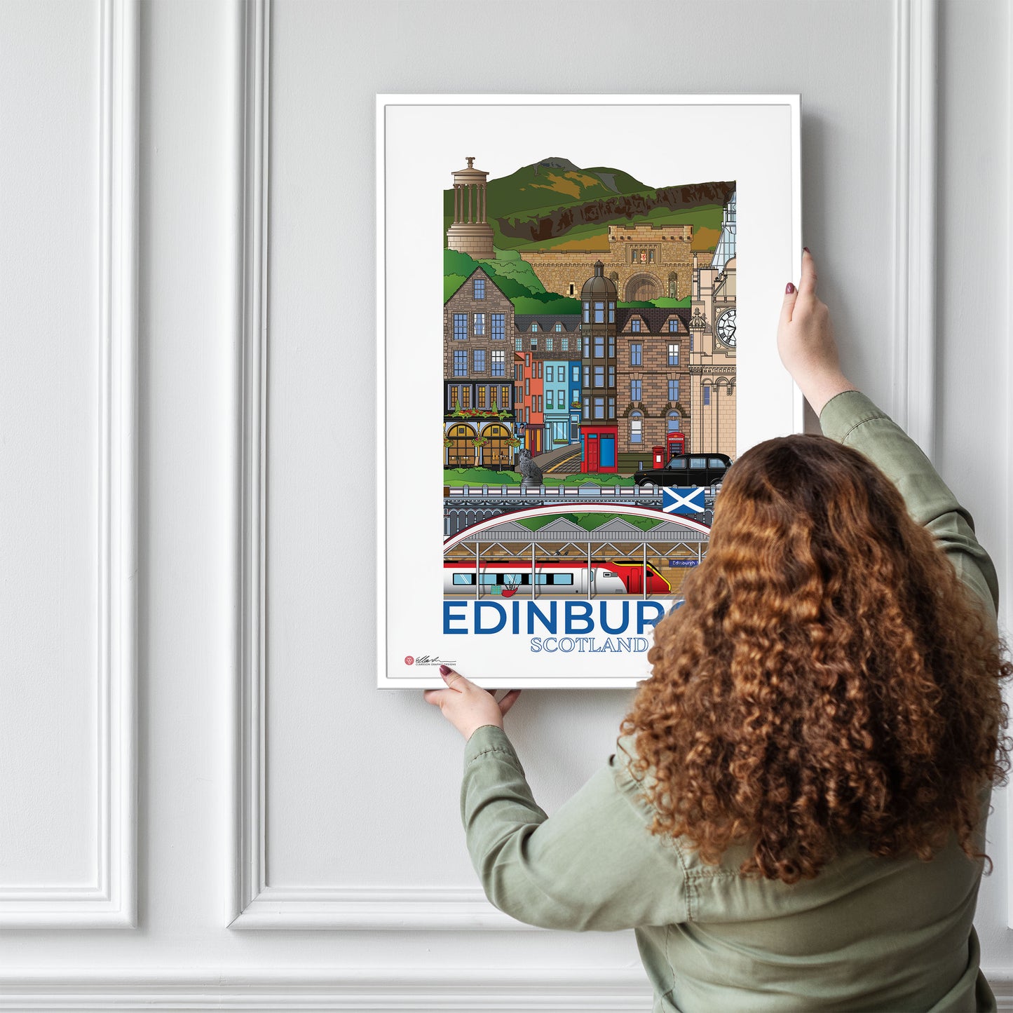 Person hanging a framed poster of Edinburgh, Scotland on a wall.