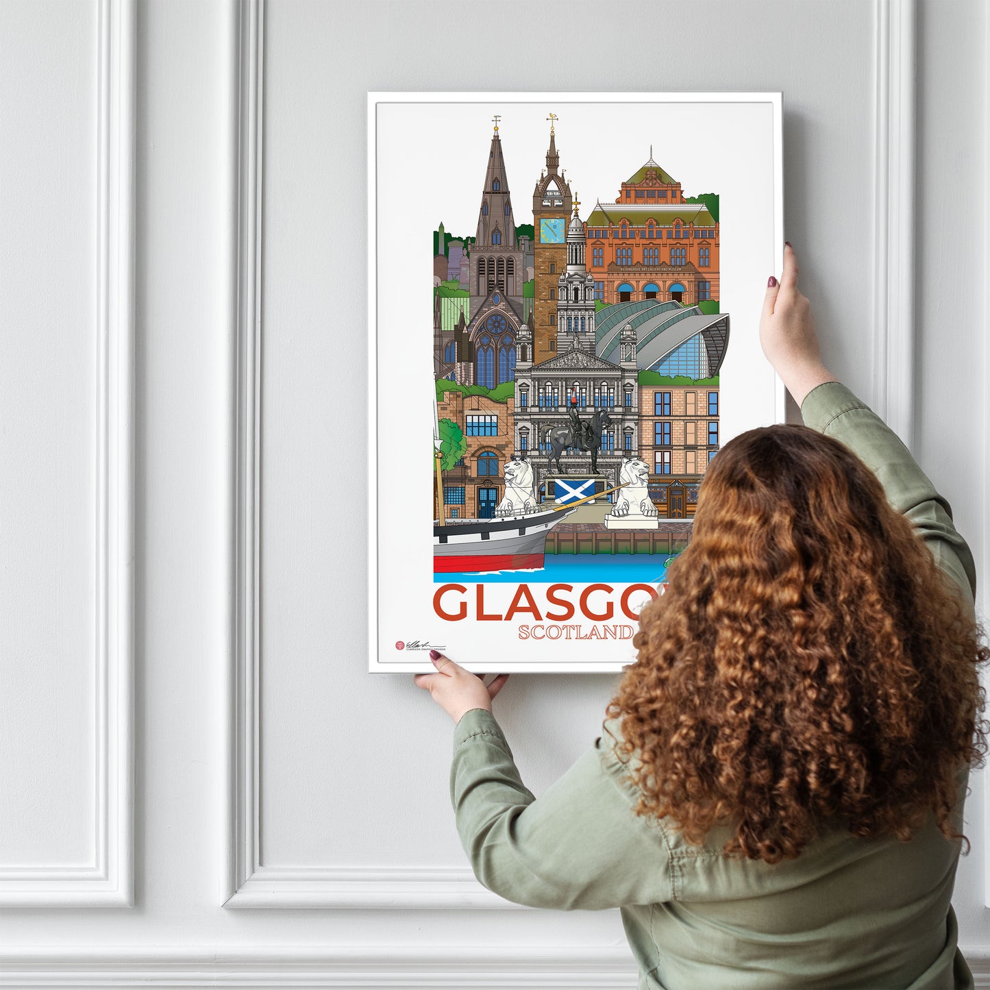 Person hanging a poster of Glasgow, Scotland on a wall.